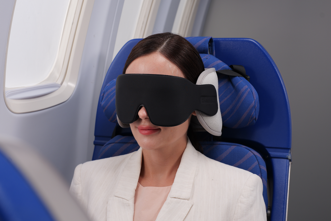 Traveler wearing an eye mask while resting in an airplane seat beside the window